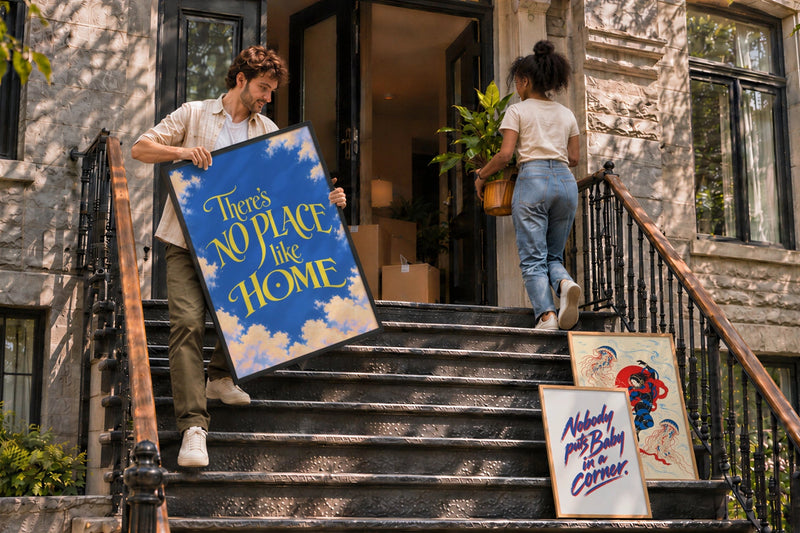 Una coppia si trasferisce in una casa a schiera in pietra e porta su per i gradini d’ingresso un poster incorniciato e una pianta, mentre altre due cornici sono appoggiate alla ringhiera.