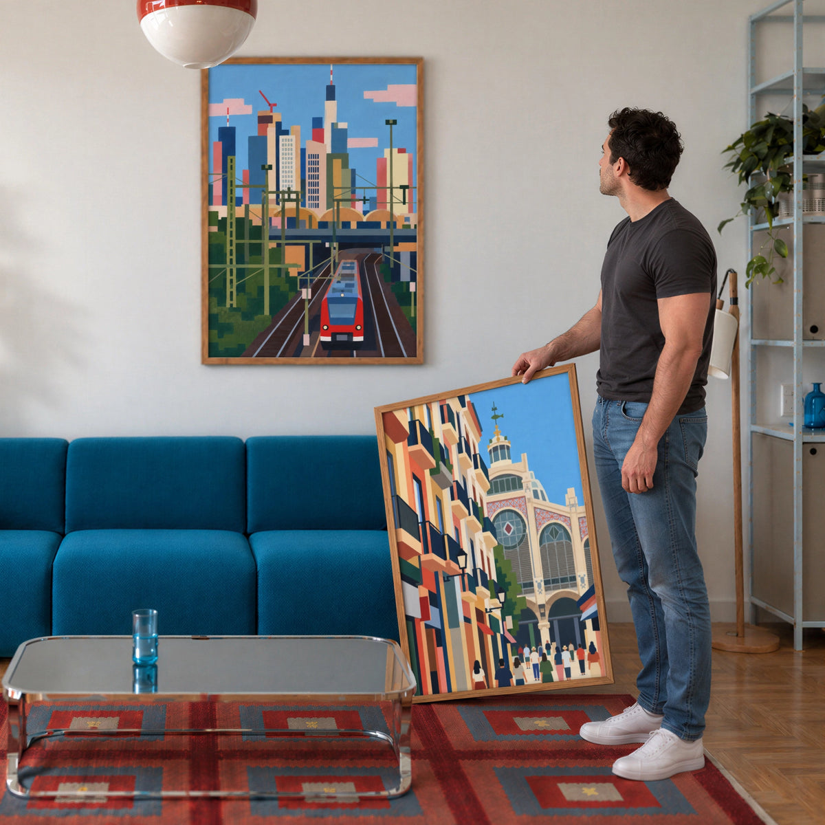 A man looks at a framed pixel-art city print with a red train above a teal sofa, holding a second framed print.