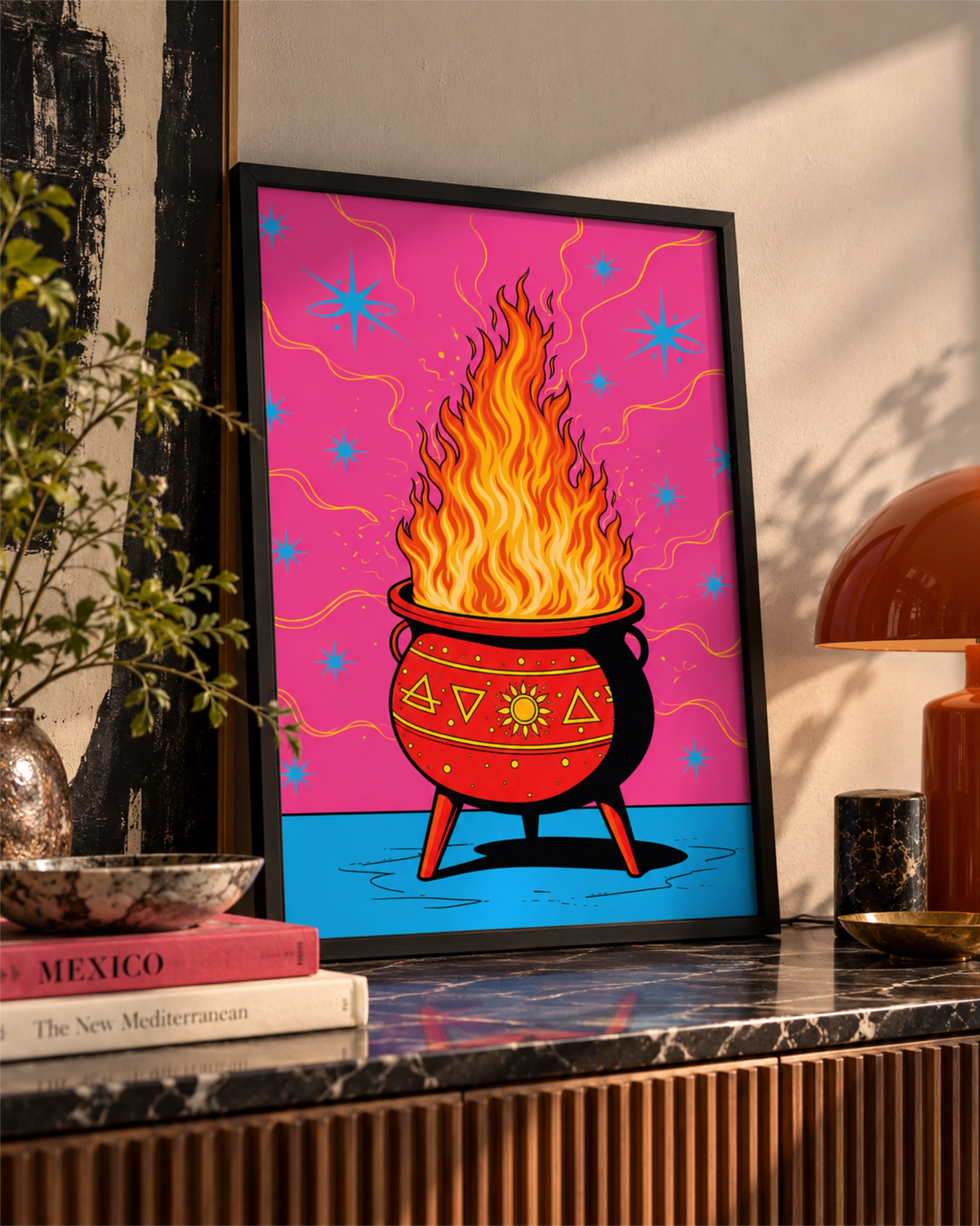 Hot Spell art print in a black frame leaning on a marble sideboard beside an orange lamp and indoor greenery.
