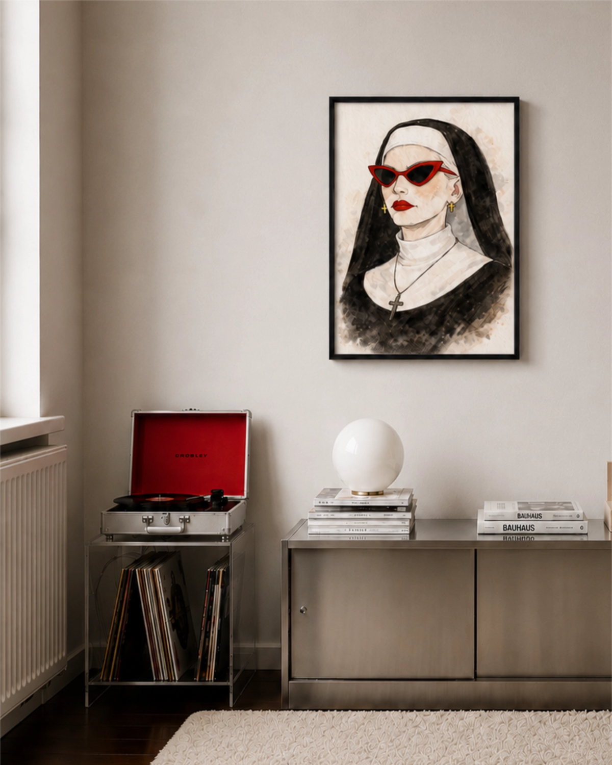 Affiche encadrée d'une religieuse aux lunettes de soleil rouges, accrochée sur un mur beige dans une pièce moderne avec buffet métallique, tourne-disque et lampe blanche.