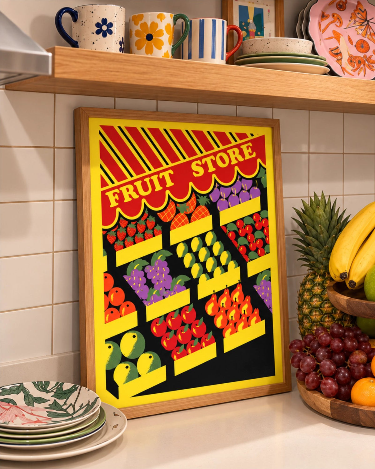 Lámina Fresh Pick con marco de madera natural en una encimera junto a platos estampados, tazas de colores y fruta fresca