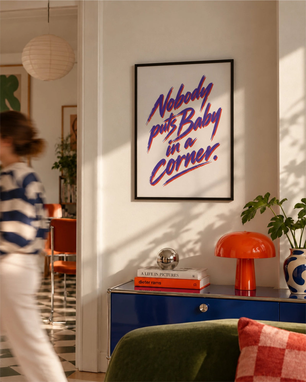 Nobody Puts Baby in a Corner poster in a black frame above a blue cabinet with an orange mushroom lamp and indoor plant in a colourful modern living room.