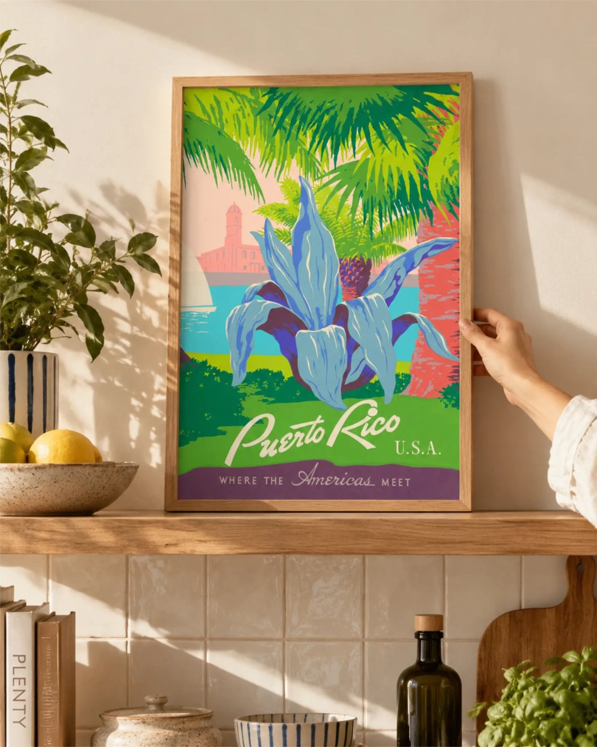 Affiche de voyage vintage Discover Puerto Rico en cadre en bois naturel sur une étagère de cuisine avec plantes et céramiques