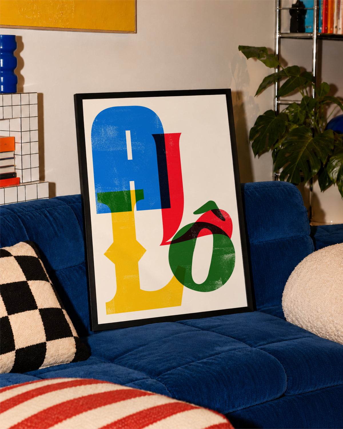 Black-framed Allô poster leaning against a vivid blue sofa with patterned cushions